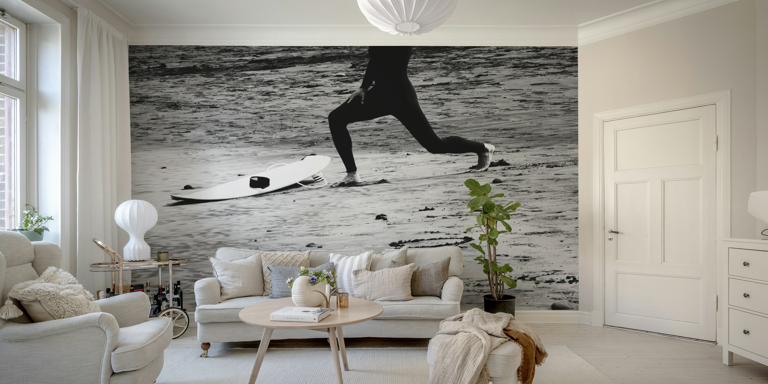 Et svart-hvitt veggmaleri som viser den dynamiske silhuetten til en surfer med brettet på stranden.